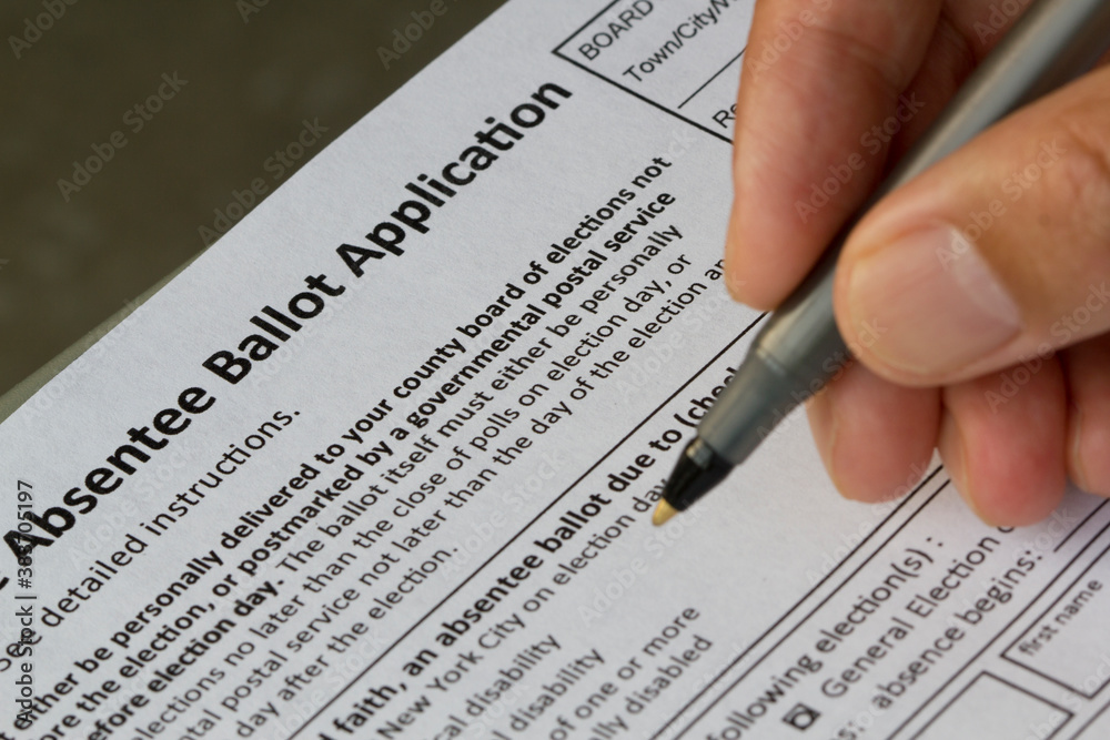 Hand holding a pen and filling out a New York State Absentee Ballot Application form. Selective focus on the form. Hand holding a pen and filling out a New York State Absentee Ballot Application form. Selective focus on the form.
