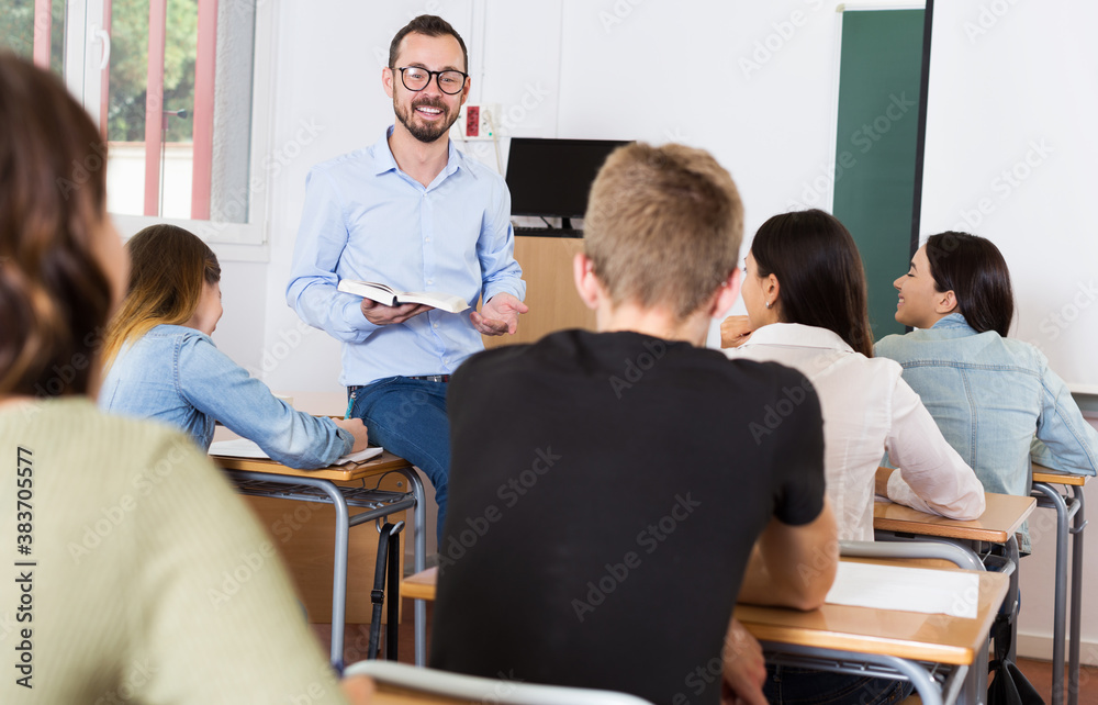 happy adult teacher is giving lecture for students with book in the class.