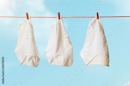 Three white women s panties on a clothesline against a blue sky.