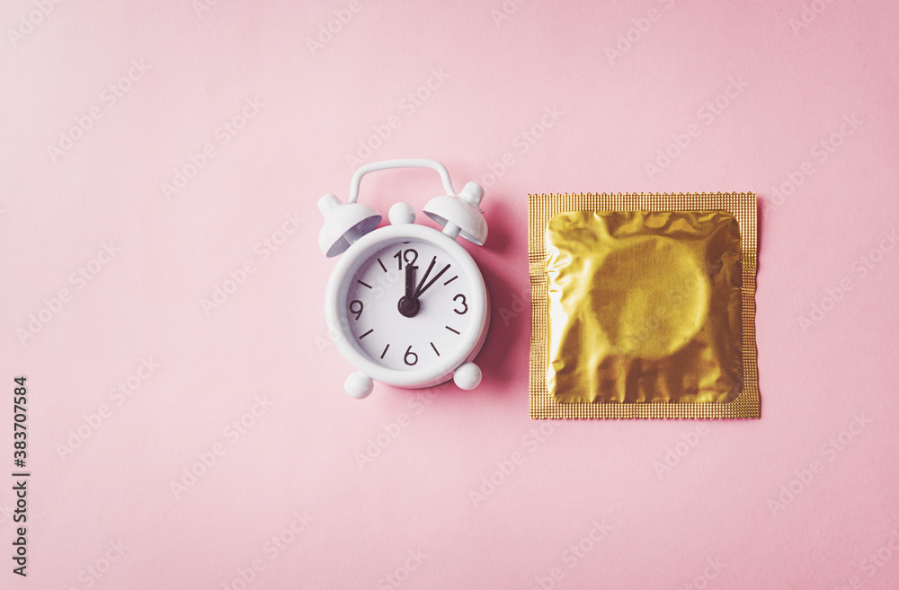 World sexual health or Aids day, condom in wrapper pack and Alarm clock birth control, studio shot isolated on a pink background, Safe sex and reproductive health concept World sexual health or Aids day, condom in wrapper pack and Alarm clock birth control, studio shot isolated on a pink background, Safe sex and reproductive health concept