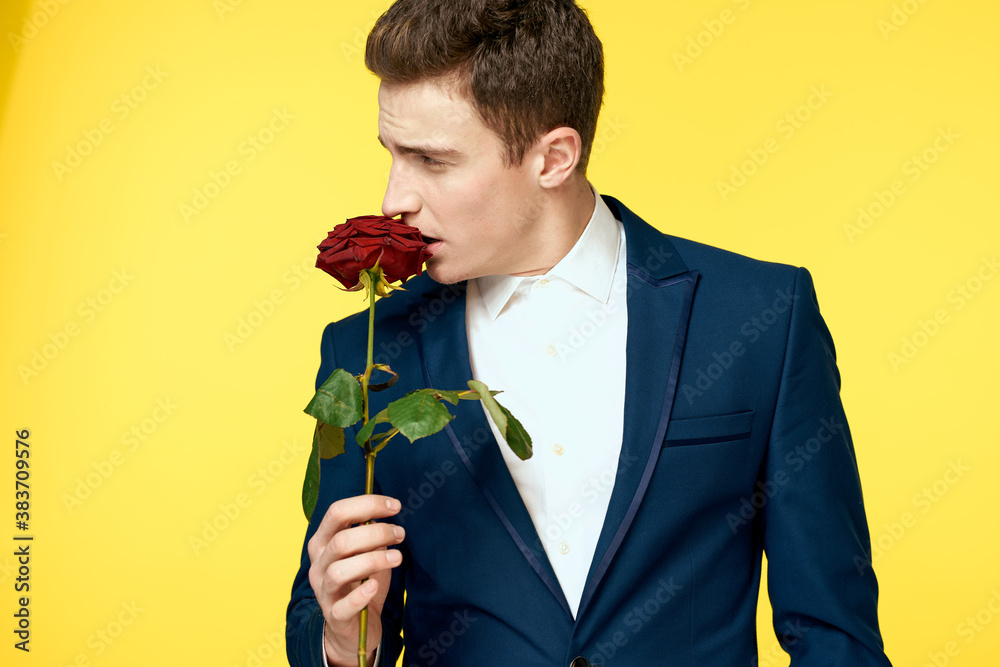 Young man in a classic suit with a red rose in his hand on a yellow background emotions cropped view model Young man in a classic suit with a red rose in his hand on a yellow background emotions cropped view model