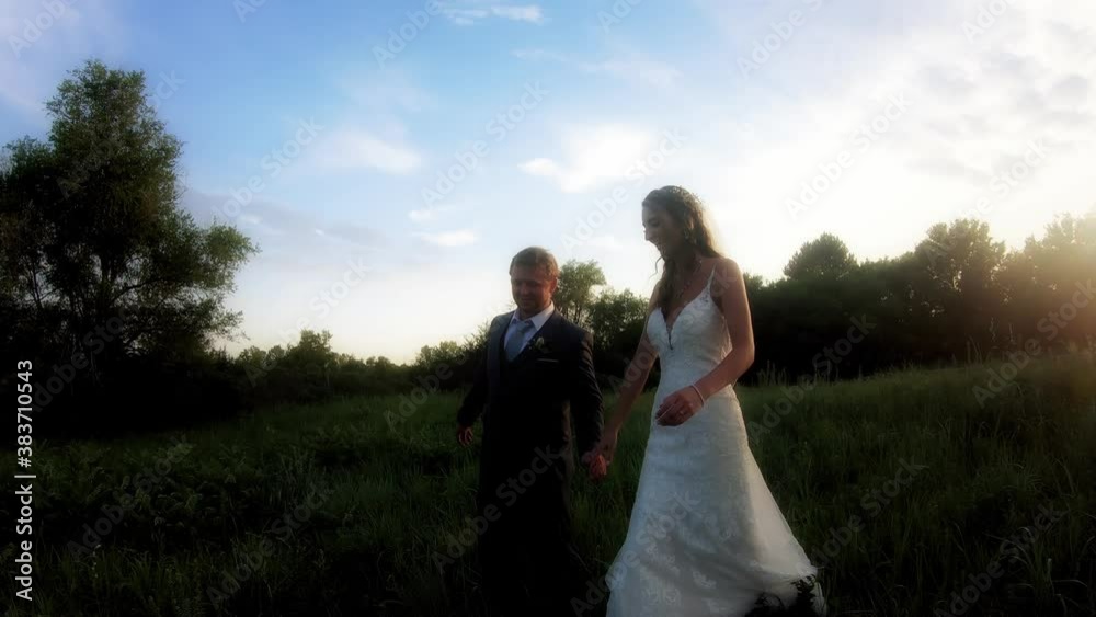 A bride and groom hold hands and smile at each other as they walk down a grassy hill after their Kansas wedding A bride and groom hold hands and smile at each other as they walk down a grassy hill after their Kansas wedding