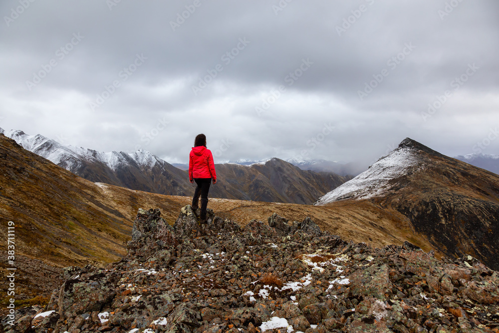 Woman Standing on Rocks looking at Scenic Mountain Peak in Canadian Nature. Season change from Fall to Winter. Taken in Tombstone Territorial Park, Yukon, Canada.