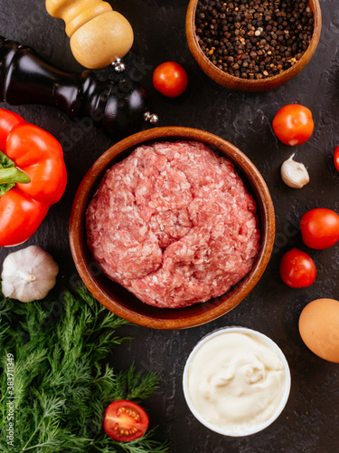 fresh raw minced pork in a wooden bowl with vegetables on the ba