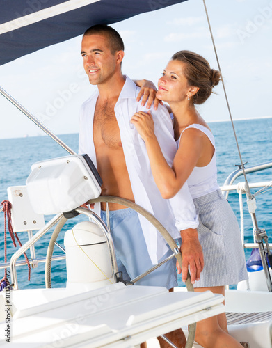 Young man and woman steering pleasure yacht, enjoying romantic sea travel on warm summer day