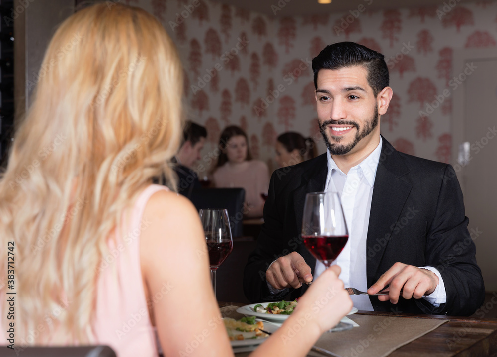 Young happy cheerful handsome man with girlfriend enjoying evening meal in cozy restaurant