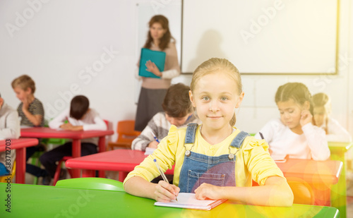 Portrait of diligent schoolgirl writing exercises at lessons in primary school.