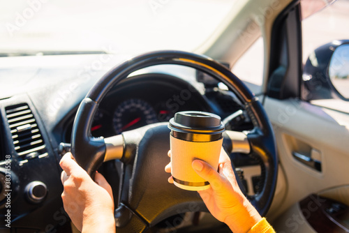 Asian woman drinking hot coffee takeaway cup inside a car and while driving the car in the morning during going to work on highway, Transportation and vehicle concept © sorapop