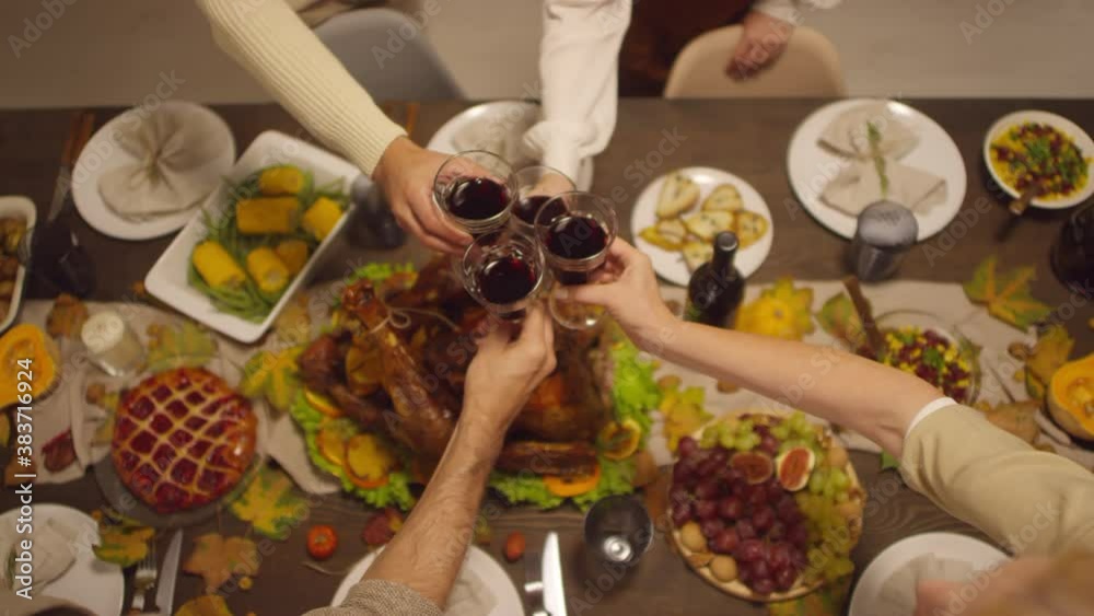 Top view shot footage of unrecognizable people clinking glasses with wine above dining table full of delicious food for Thanksgiving celebration