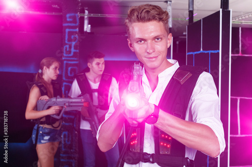 Portrait of smiling young guy holding laser pistol playing laser tag game with his friends