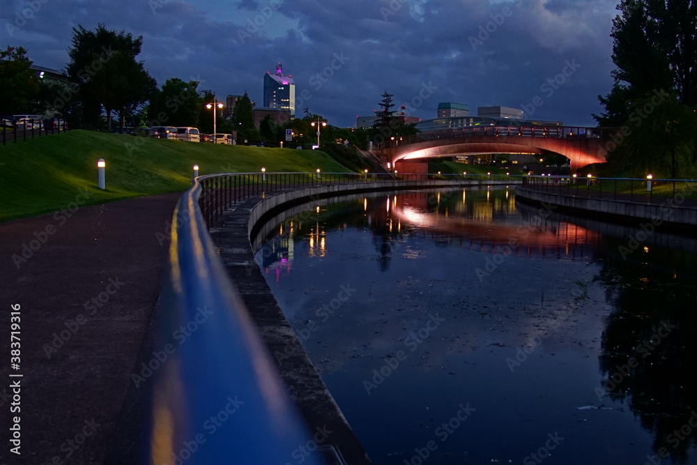 City night park in early autumn with pavement, young green leaves and trees and river. Landscape, Japan. City night park in early autumn with pavement, young green leaves and trees and river. Landscape, Japan.