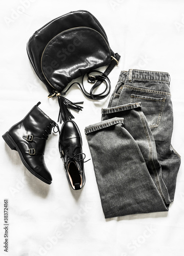 Grey jeans, black leather shoes, black leather bag - women's clothing on a light background, top view. Fashion concept