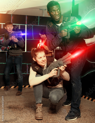 Nice laser tag players of different nationalities aiming laser guns at other players during lasertag game in dark room