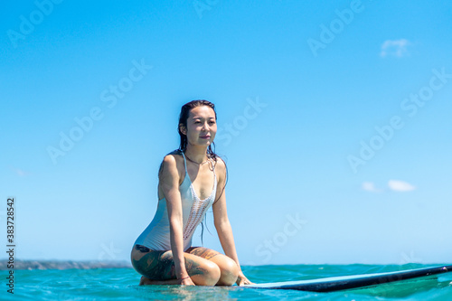 Portrait of surfer girl on surf board in blue ocean . © Lila Koan
