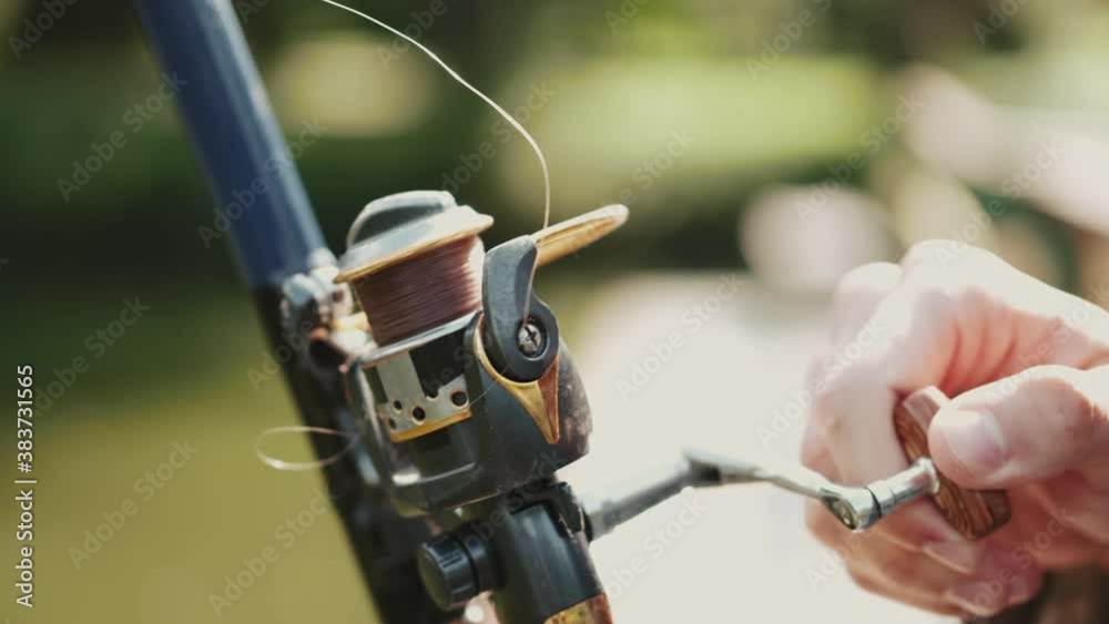 Closeup of fisher holding a spinning and pulling on the thread. The man is fishing at the pond in a park. Fishing hobby. Closeup of fisher holding a spinning and pulling on the thread. The man is fishing at the pond in a park. Fishing hobby.