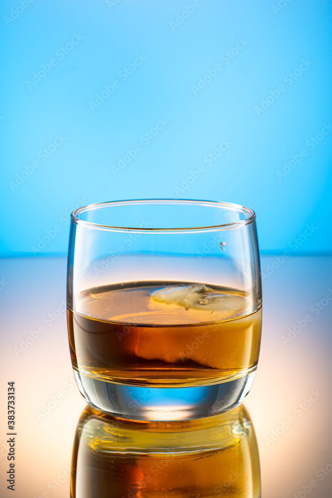 whiskey with ice splash in a glass on a colored gradient background