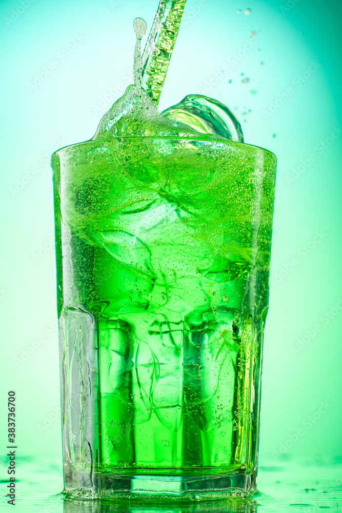 pouring green tarragon lemonade into glass with pieces of pure real ice on green gradient background pouring green tarragon lemonade into glass with pieces of pure real ice on green gradient background