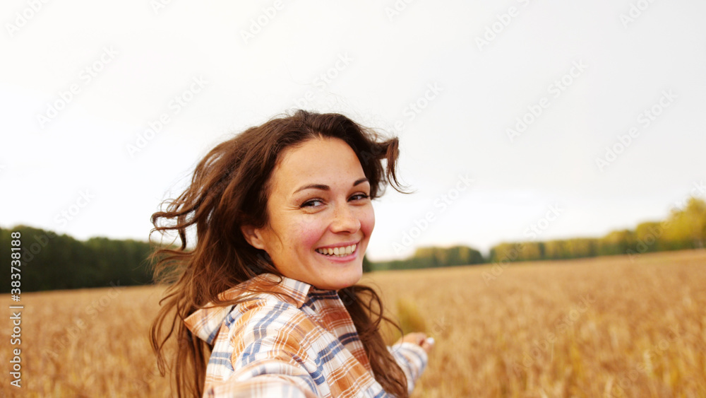 Brunette pretty woman leads across a field of ripe wheat turning smiling. follow me concept