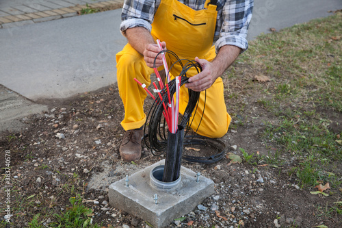 Worker installing optic fiber cables for internet and telephone, power lines installation at street