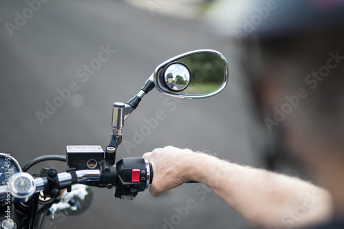 View of a male active senior man riding his bike looking down at the handlebars of his motorbike cycle chrome guages mirros hand instrumentation outdoors on a bright day