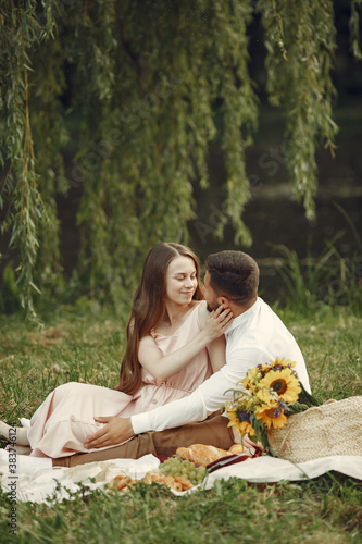 Couple in a field. Brunette in a white dress. Pair sitting on a grass.