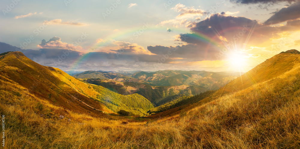 mountain landscape in autumn at sunset. dry colorful grass on the hills. ridge behind the distant valley in evening light. view from the top of a hill. clouds on the sky