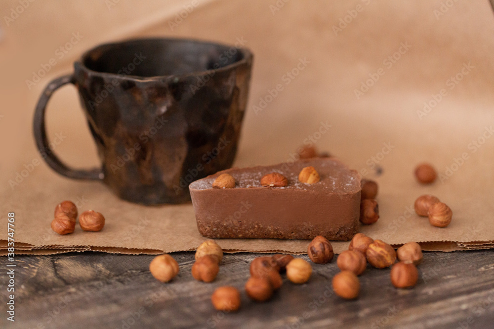 Chocolate cheesecake on a wooden Board with scattered hazelnuts and a clay Cup