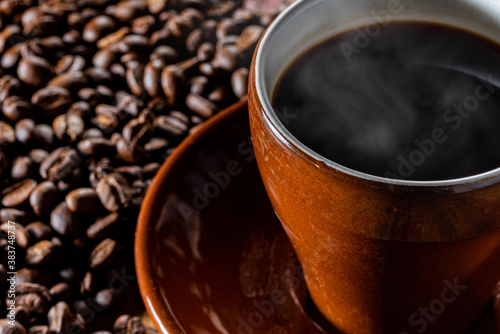 カップに入った湯気の立つ熱いコーヒーと背景のコーヒー豆