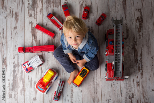 Foto Child, toddler blond boy, playing with fire trucks on the floor