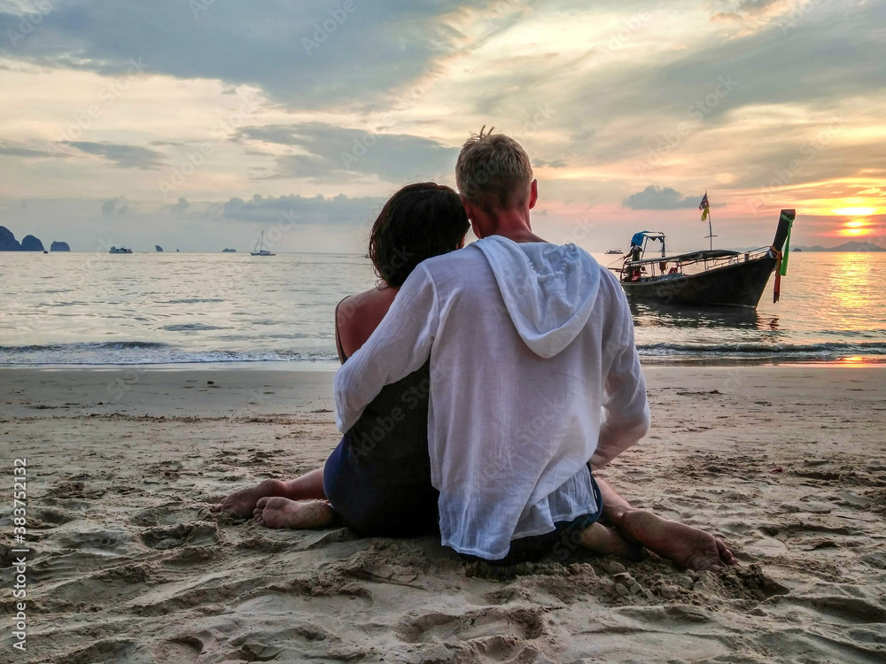 Fototapeta premium Sunset, sandy beach, couple in love sitting in an embrace at sunset on the beach on vacation