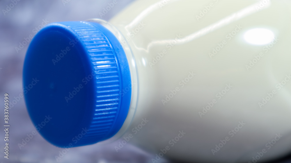 A plastic bottle with a blue cap of fresh regular milk on a dark gray marbled or concrete background. Close-up front view. World milk day concept. Nutrient fluid.