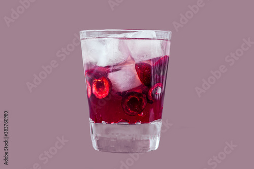 Fresh cherry cocktail. A cocktail with gin or vodka, cherry syrup and pieces cherry and ice in a whiskey glass. Glass of drink isolated on purple background