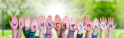 Children Hands Building Colorful German Word Weihnachtsmann Means Santa Claus. Sunny Green Grass Meadow As Background