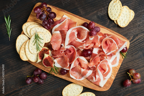 Italian bacon prosciutto crudo or spanish jamon with grapes and crackers on a wooden plate. Food for an aperitif and dinner lunch in the restaurant. food delivery home