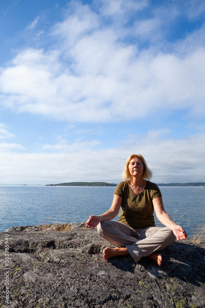 Seinor woman relaxing and meditating outdoors by the sea on a summer day