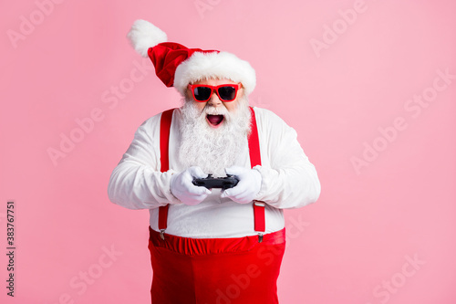 Portrait of his he nice cheerful cheery glad focused bearded fat guy Santa father playing console station contest network battle competition air blow wind contest isolated pink pastel color background