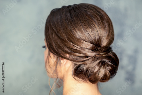 Rear view of young brunette woman with beautiful middle bun hairstyle on gray background