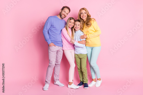Full size photo of positive family dad hug mom and two kids boy girl isolated over pink color background