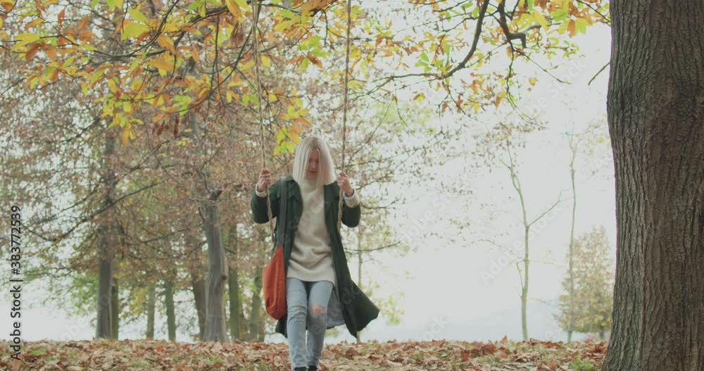Beautiful woman swinging under a big tree in a cold autumn journey. Back to childhood. slow motion Beautiful woman swinging under a big tree in a cold autumn journey. Back to childhood. slow motion