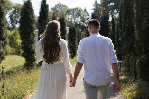 a guy and a girl in white clothes hold hands and walk in the park © Roman
