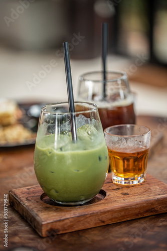 Green Matcha Latte in glass cup served with hot tea on wooden board.