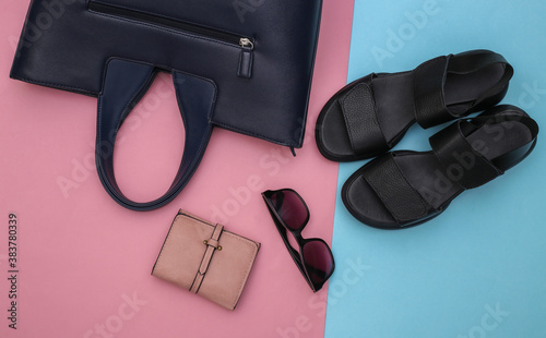 Flat lay style womens accessories on pink pastel background. Sandals, bag, leather wallet and sunglasses. Top view