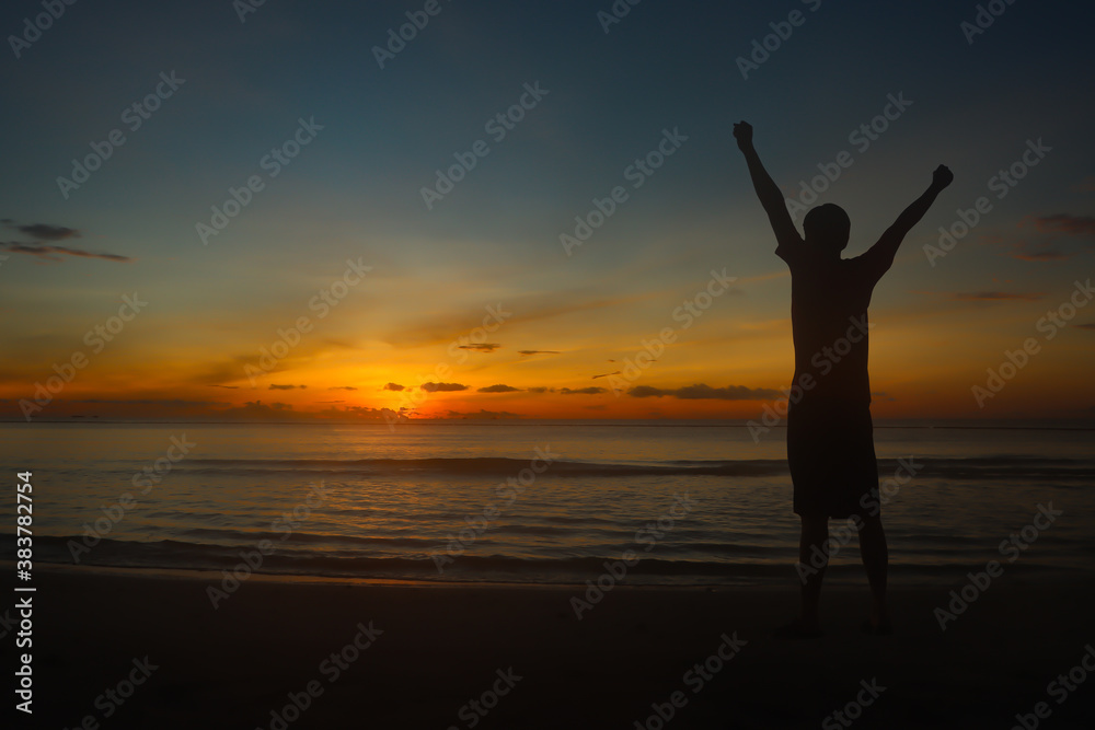 Silhouette man  raise their arms on the beach in morning with sun rise.