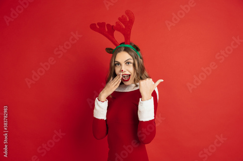 Pointing. Greetingcard. Concept of Christmas, 2021 New Year's, winter mood, holidays. Copyspace for ad, postcard. Beautiful caucasian woman with long hair like Santa's Reindeer catching giftbox.
