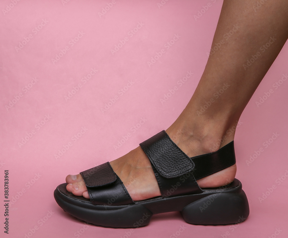 Female feet in fashionable leather sandals on a pink background