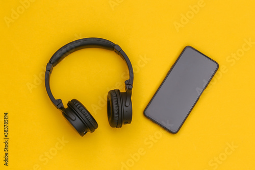 Wireless stereo headphones and smartphone on yellow background. Top view