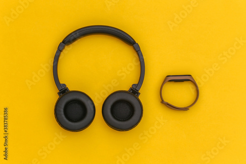 Wireless stereo headphones and smart bracelet on a yellow background. Modern gadgets. Top view