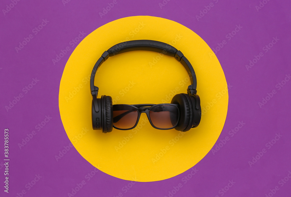Stereo headphones with sunglasses on a purple background with a yellow circle. Top view Stereo headphones with sunglasses on a purple background with a yellow circle. Top view