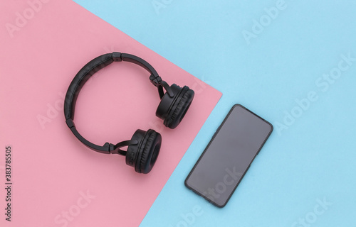 Smartphone and wireless stereo headphones on pink blue pastel background. Top view