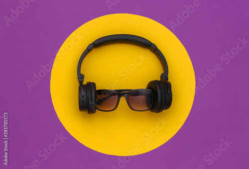 Stereo headphones with sunglasses on a purple background with a yellow circle. Top view